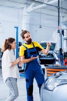 Adept repairman in repair shop using holographic AR technology to show customer car performance parameters. Garage worker using futuristic vr headset to inform client of issues found in vehicle