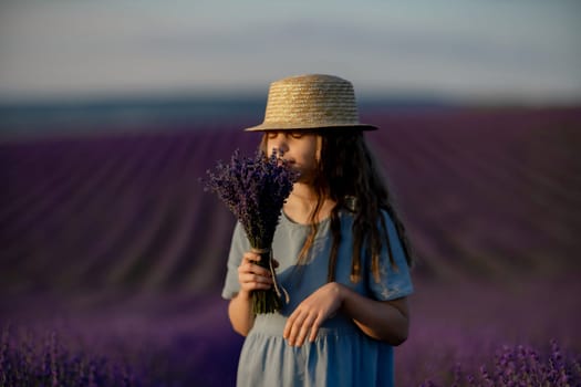 Lavender sunset girl. A laughing girl in a blue dress with flowing hair in a hat walks through a lilac field, holds a bouquet of lavender in her hands