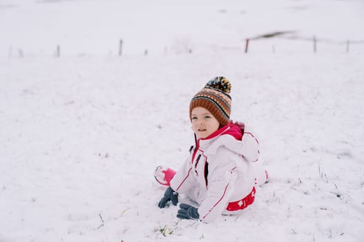 Little smiling girl sits half-turned on the snow. High quality photo