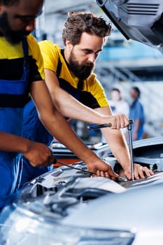 Technicians collaborating on servicing broken vehicle, checking for faulty ignition system. Meticulous repairmen in auto repair shop working together on fixing automobile, discussing best options