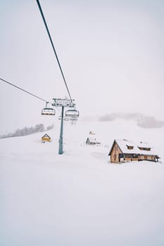 Chairlift passes by wooden cottages on a snow-capped mountain. High quality photo