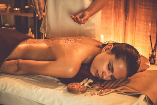 Woman customer having exfoliation treatment in luxury spa salon with warmth candle light ambient. Salt scrub beauty treatment in Health spa body scrub. Quiescent