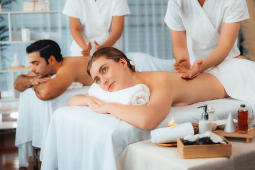 Caucasian couple customer enjoying relaxing anti-stress spa massage and pampering with beauty skin recreation leisure in day light ambient salon spa at luxury resort or hotel. Quiescent