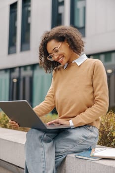 Pretty female entrepreneur working on laptop sitting outside on modern building background