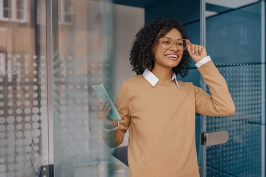 Smiling female freelancer holding phone while standing on coworking background