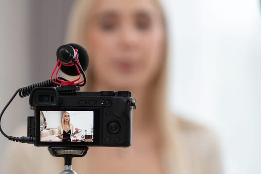 Blurred young woman making beauty and cosmetic tutorial video content for social media. Focused camera screen with beauty influencer showing how to apply beauty care to audience or followers. Blithe