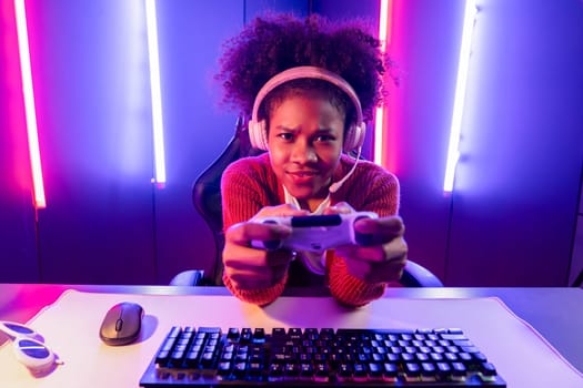 Host channel of gaming streamer, African girl playing online game with joystick, talking with viewers media online on microphone. Esport skilled team players in neon color lighting room. Tastemaker.