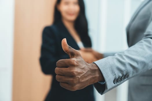 Closeup image of african businessman hand showing thump up to camera while young businesswoman standing behind. Represent recommend, support, good, positive, professional, reliable. Ornamented.