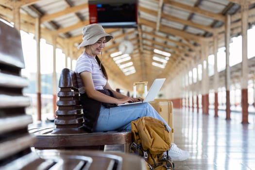 Woman traveler with backpack using laptop to planning vacation on holiday relaxation at the train station.