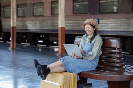 Woman traveler with backpack using laptop to planning vacation on holiday relaxation at the train station.