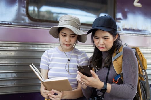 two women traveler friends are at the train station checking the map of the city on mobile.