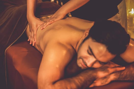 Caucasian man customer enjoying relaxing anti-stress spa massage and pampering with beauty skin recreation leisure in warm candle lighting ambient salon spa at luxury resort or hotel. Quiescent