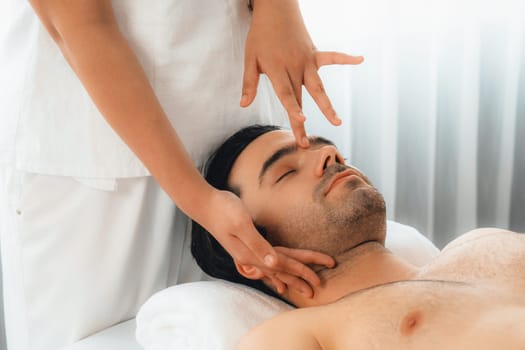 Caucasian man enjoying relaxing anti-stress head massage and pampering facial beauty skin recreation leisure in dayspa modern light ambient at luxury resort or hotel spa salon. Quiescent