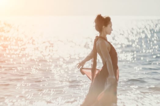 Side view a Young beautiful sensual woman in a red long dress posing on a rock high above the sea during sunrise. Girl on the nature on blue sky background. Fashion photo.