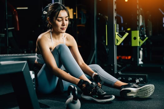 Asian woman tying her shoelace while resting on the floor after a yoga session. The shot highlights her athletic shoes and sporty leggings.