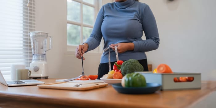 Young woman asian measure her waist in the kitchen the with vegetables and fruits. Concept of healthy eating and dieting.