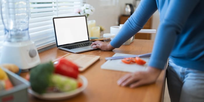 Cheerful Fat woman cooking in kitchen showing laptop mock up blank white screen in home.