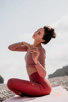 Young woman with long hair in white swimsuit and boho style braclets practicing outdoors on yoga mat by the sea on a sunset. Women's yoga fitness routine. Healthy lifestyle, harmony and meditation