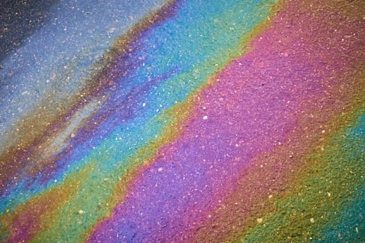 Background texture of an oil spill in the form of a rainbow stain on dark asphalt, parking..