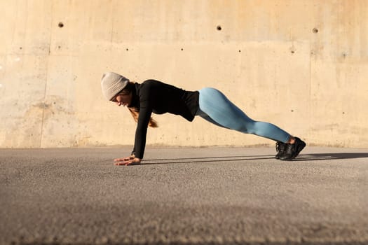 Side view of young female wearing sportswear doing plank plank pose outdoors in winter. Active and healthy lifestyle concept.