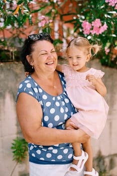 Laughing granny with a little girl in her arms stands near a flowering tree. High quality photo