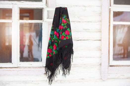 Russian national scarf hangs on the window of a wooden house..