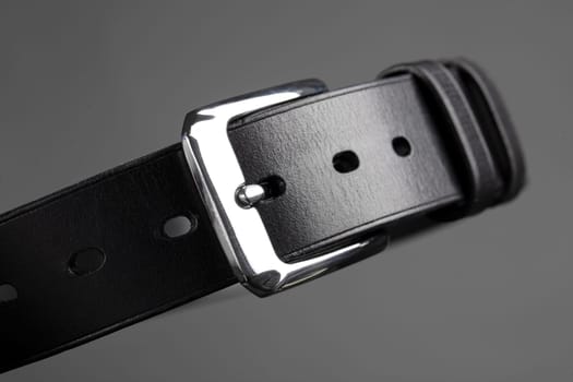 Part of a black leather belt with a metal buckle close-up on a gray background.