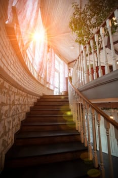 A spiral staircase with wooden railings leads up to the top illuminated by the sun.