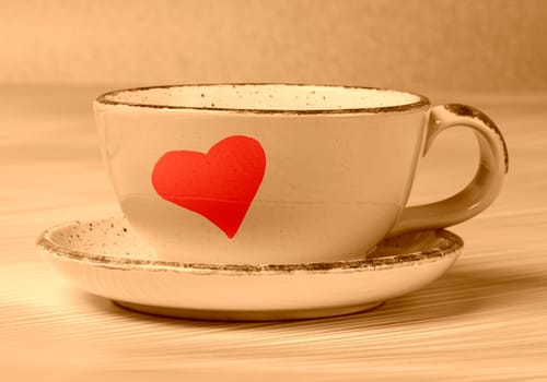 Ceramic cup with painted red heart in beige toning. Morning coffee or tea with love.