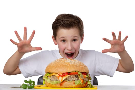 Young eccentric boy with a big hamburger isolated in white. The teenager shows a good appetite.