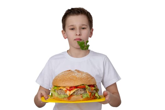 Young boy with big hamburger isolated in white. A teenager is holding a burger and a bunch of parsley.
