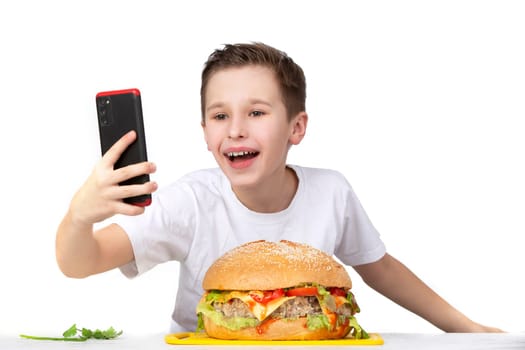 A young boy takes a selfie with a big hamburger, isolated in white.