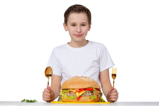 Young boy with big hamburger isolated in white. A teenager holds a golden fork and a spoon.