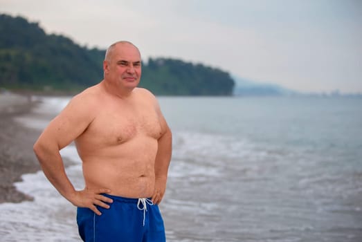 An elderly man of athletic build on the background of the sea.