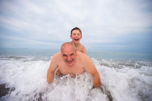 Happy boy swims and plays with grandpa on the beach.