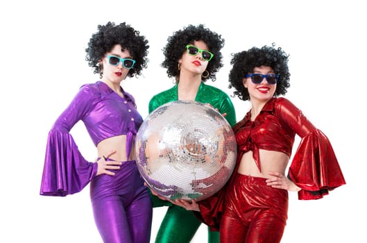 A group of girls dressed in a disco style in shiny multi-colored costumes are holding a disco ball.