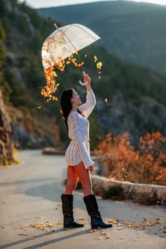 woman umbrella leaves , She holds him over her head, autumn leaves are falling out of him. Beautiful woman in a dress with an umbrella in the autumn park on the road in the mountains