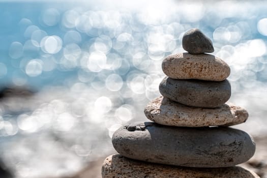 Tower of stones. Balanced pebble pyramid on the beach on a sunny day. Blue sea on the background. Selective focus, bokeh. Zen stones on the sea beach, meditation, spa, harmony, tranquility, balance concept.