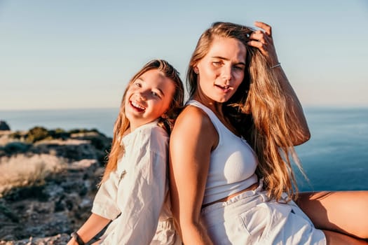 Close up portrait of mom and her teenage daughter hugging and smiling together over sunset sea view. Beautiful woman relaxing with her child.