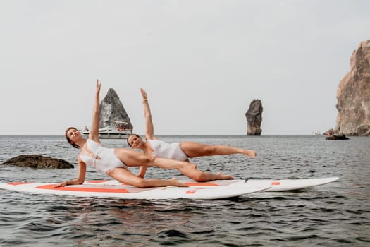 Woman sup yoga. Middle age sporty woman practising yoga pilates on paddle sup surfboard. Female stretching doing workout on sea water. Modern individual hipster outdoor summer sport activity