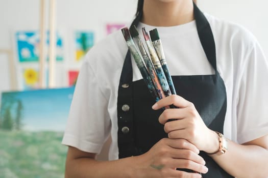 A close-up of the artist hands wearing an apron smeared with paint. Clutching many brushes and paintbrushes. Hobby and lifestyle concept.