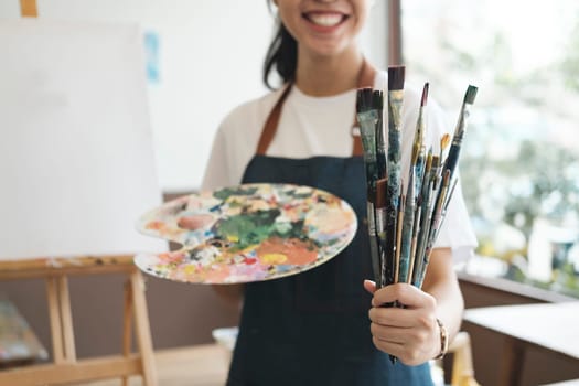 A close-up of the artist hands wearing an apron smeared with paint. Clutching many brushes and paintbrushes. Hobby and lifestyle concept.