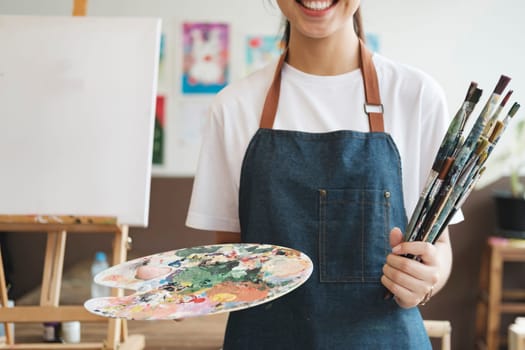 A close-up of the artist hands wearing an apron smeared with paint. Clutching many brushes and paintbrushes. Hobby and lifestyle concept.