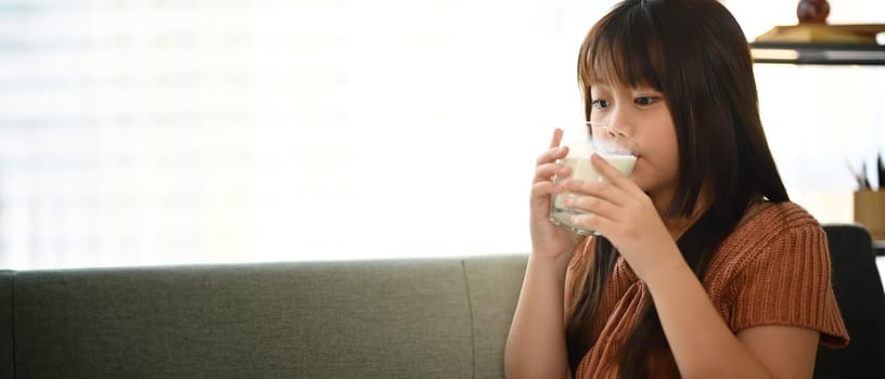 Cute little Asian girl in casual clothes drinking fresh milk. Growth and nutrition concept.