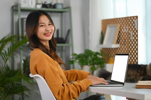 Portrait of cheerful female freelancer in yellow sweater working on laptop at home.