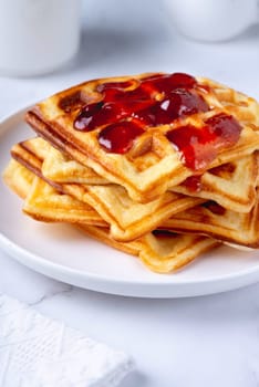 Belgian waffles with strawberry jam on a white background.