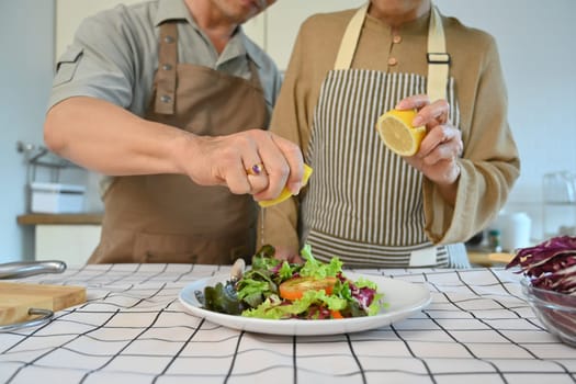 Cropped shot of senior couple squeezing fresh lemon juice into bowl with vegetable salad.