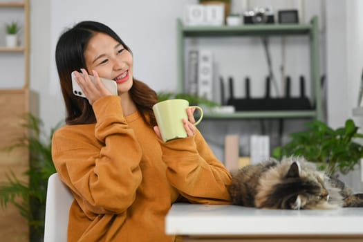 Pretty young Asian woman drinking hot tea and talking on mobile phone with friends or lover.