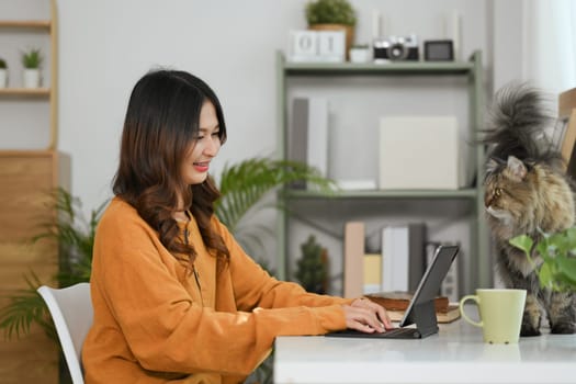 Attractive young woman in yellow sweater browsing internet on digital tablet at home.