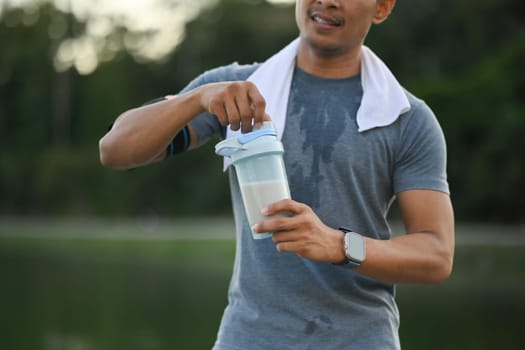 Image of athletic sportsman drinking protein shake after morning cardio workout in the park.